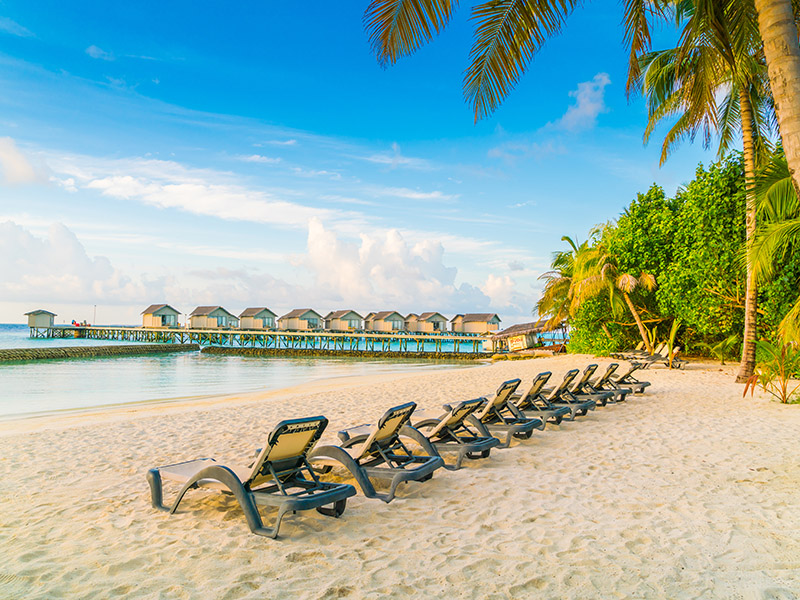 Beach chairs in Maldives island with water villas at the sunrise time